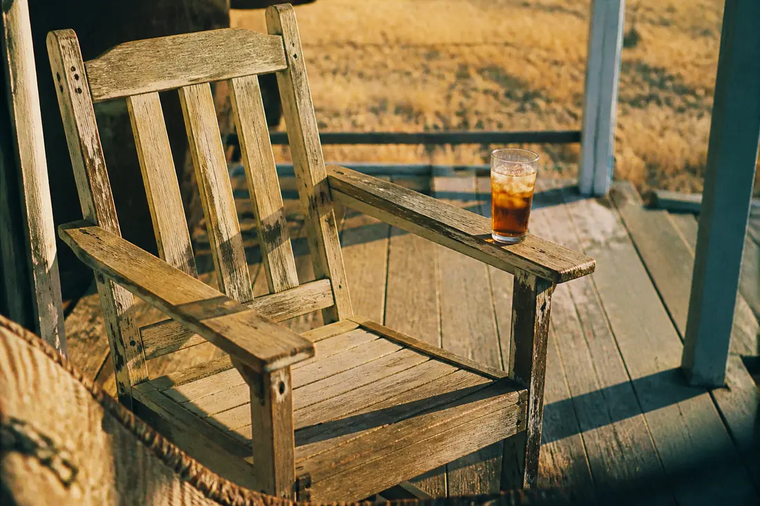An empty porch chair on sun-bleached decking in golden-hour light
